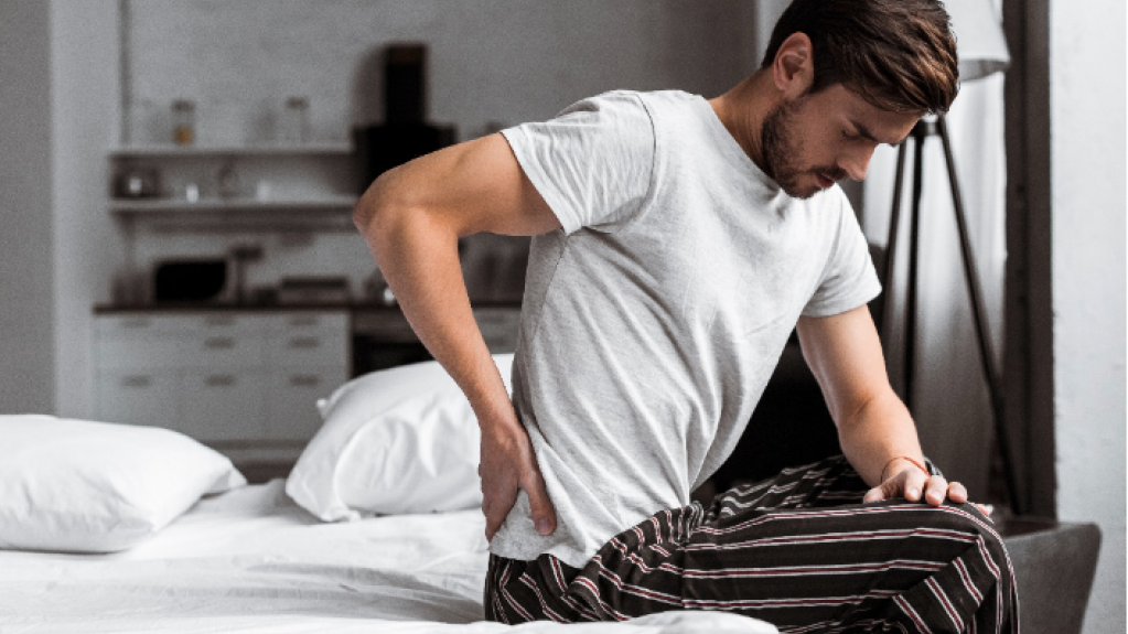 Mann sitzt auf dem Bett und hält sich den Rücken