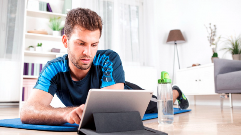 Mann liegt auf einer Sportmatte und benutzt ein Tablet für das Training